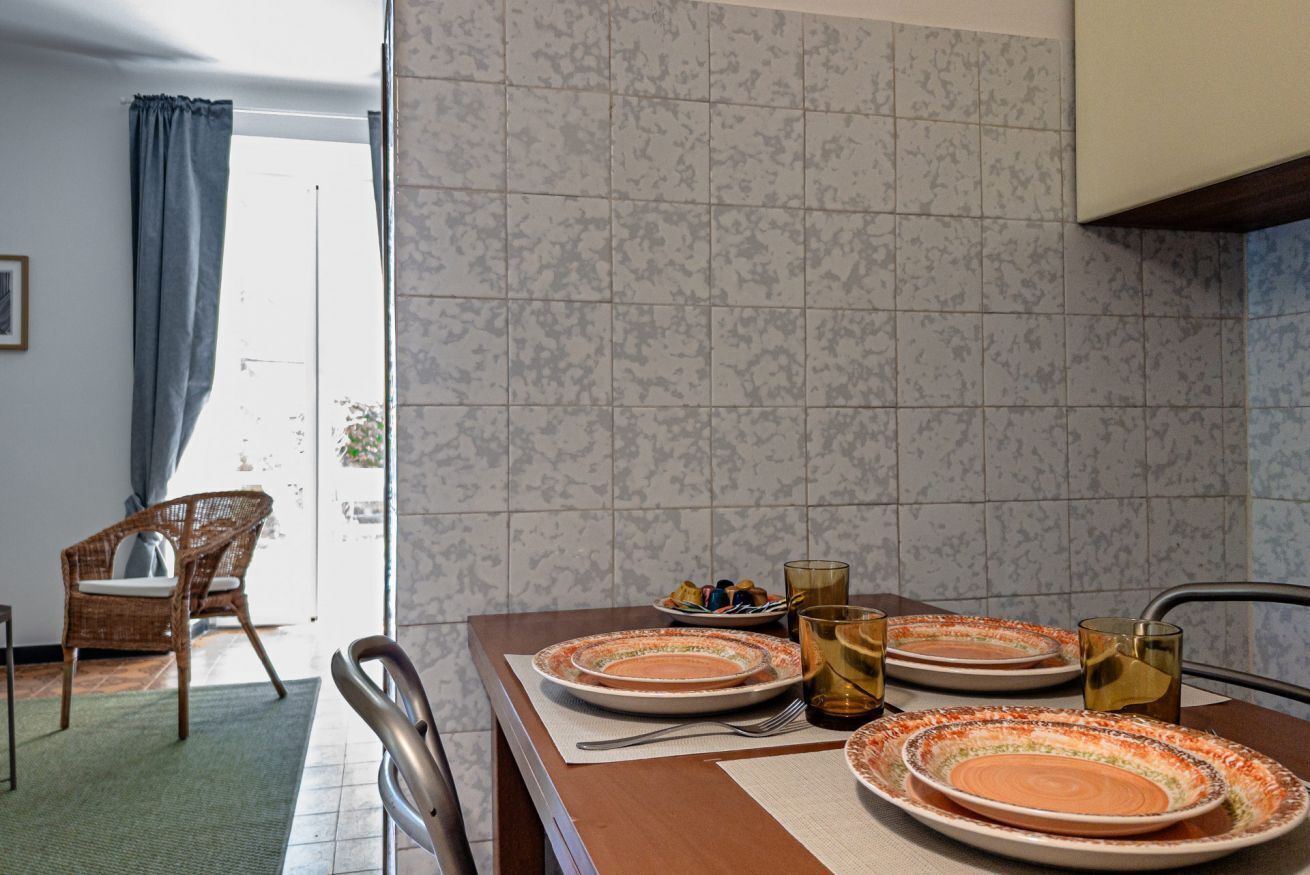 Comedor con una mesa preparada para dos, una silla de mimbre y vistas al exterior a través de una ventana.