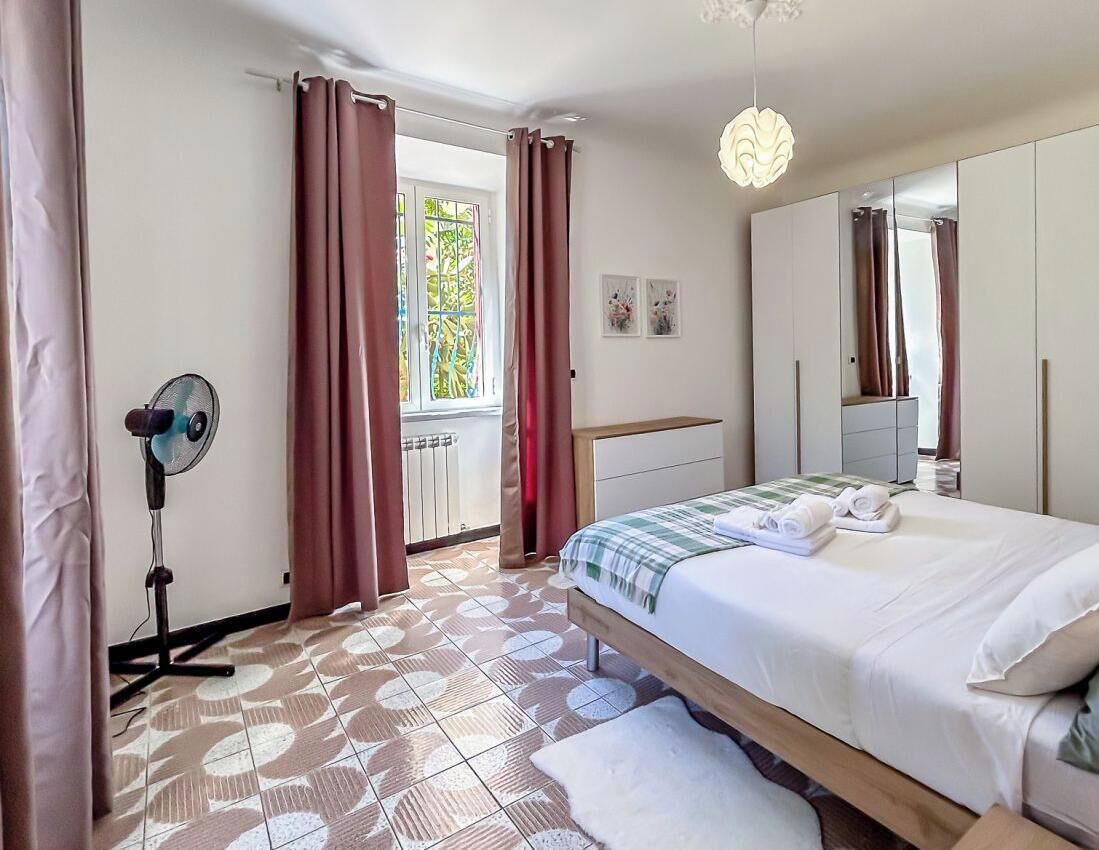 Una camera da letto con un letto, una ventola, una finestra con tende, uno specchio e una lampada a soffitto.