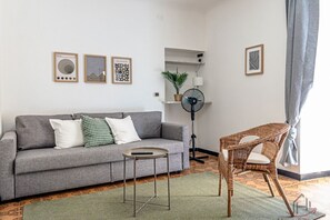 A living room with a grey sofa, a wicker chair, a small table, and a floor lamp. - [Center Refuge] Free Parking • Garden • Cruises (Savona)
