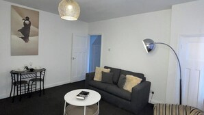 A living room with a sofa, a round coffee table, a small dining table with chairs, a lamp, and a painting on the wall. - Apartment Sleeps 2 - Free Street Parking (Gateshead)