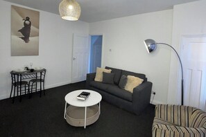 Un salon comprenant un canapé, une table basse ronde, une petite table à manger avec des chaises, une lampe et un tableau accroché au mur.