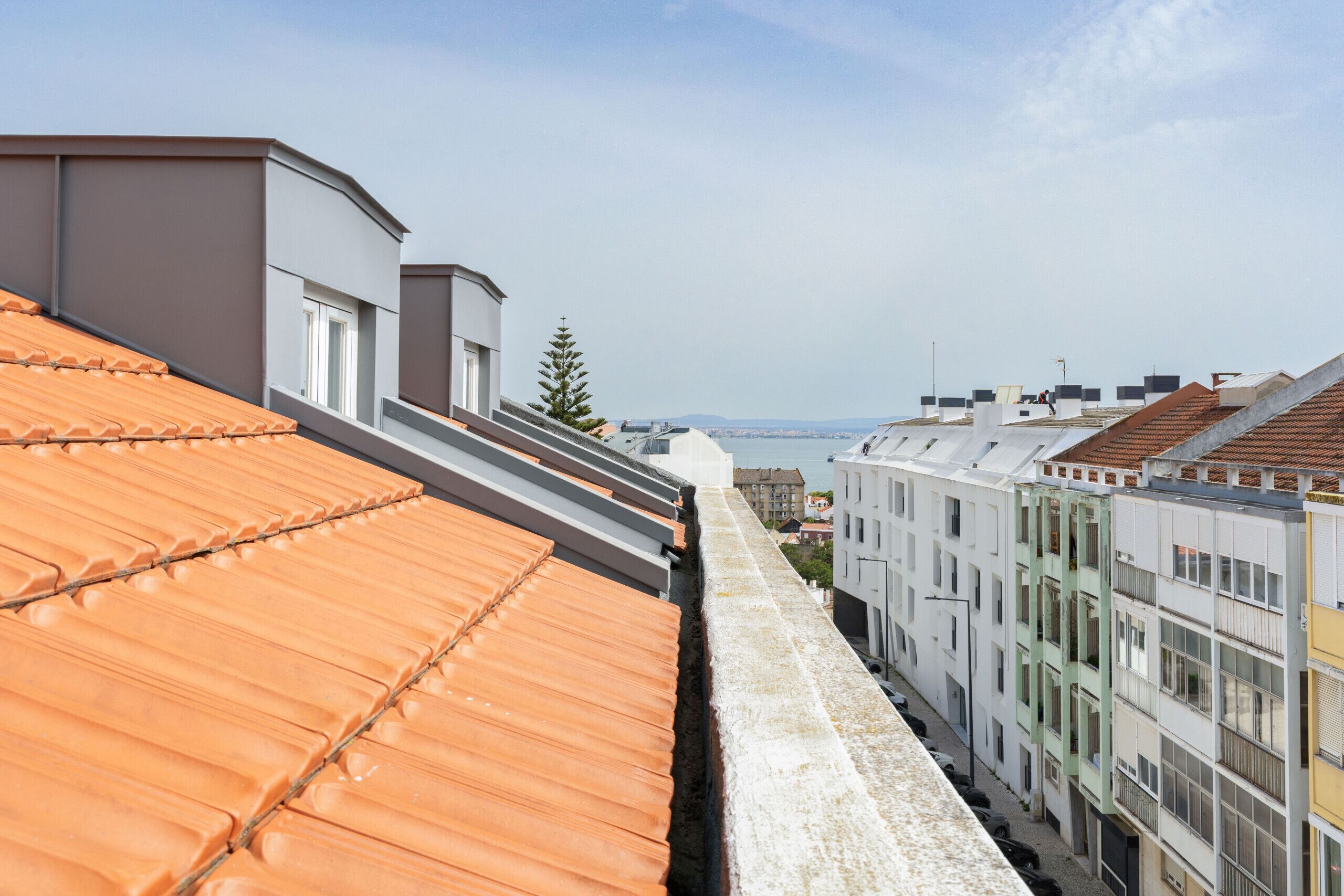 Une rangée d’immeubles modernes aux toits plats, une ruelle étroite qui les sépare, et une vue dégagée sur le paysage urbain au loin.