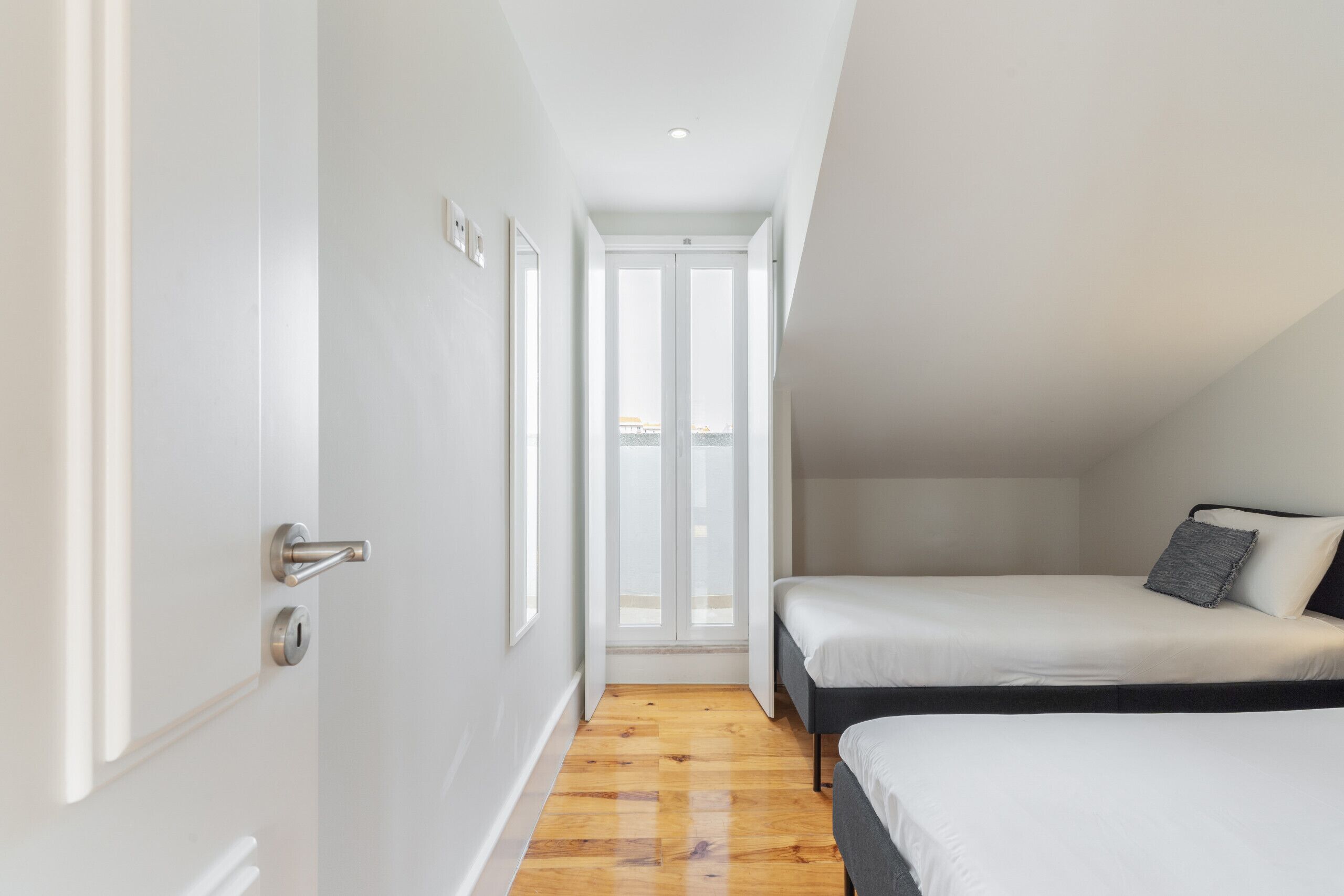 A narrow room with a door, a window, and a bed.