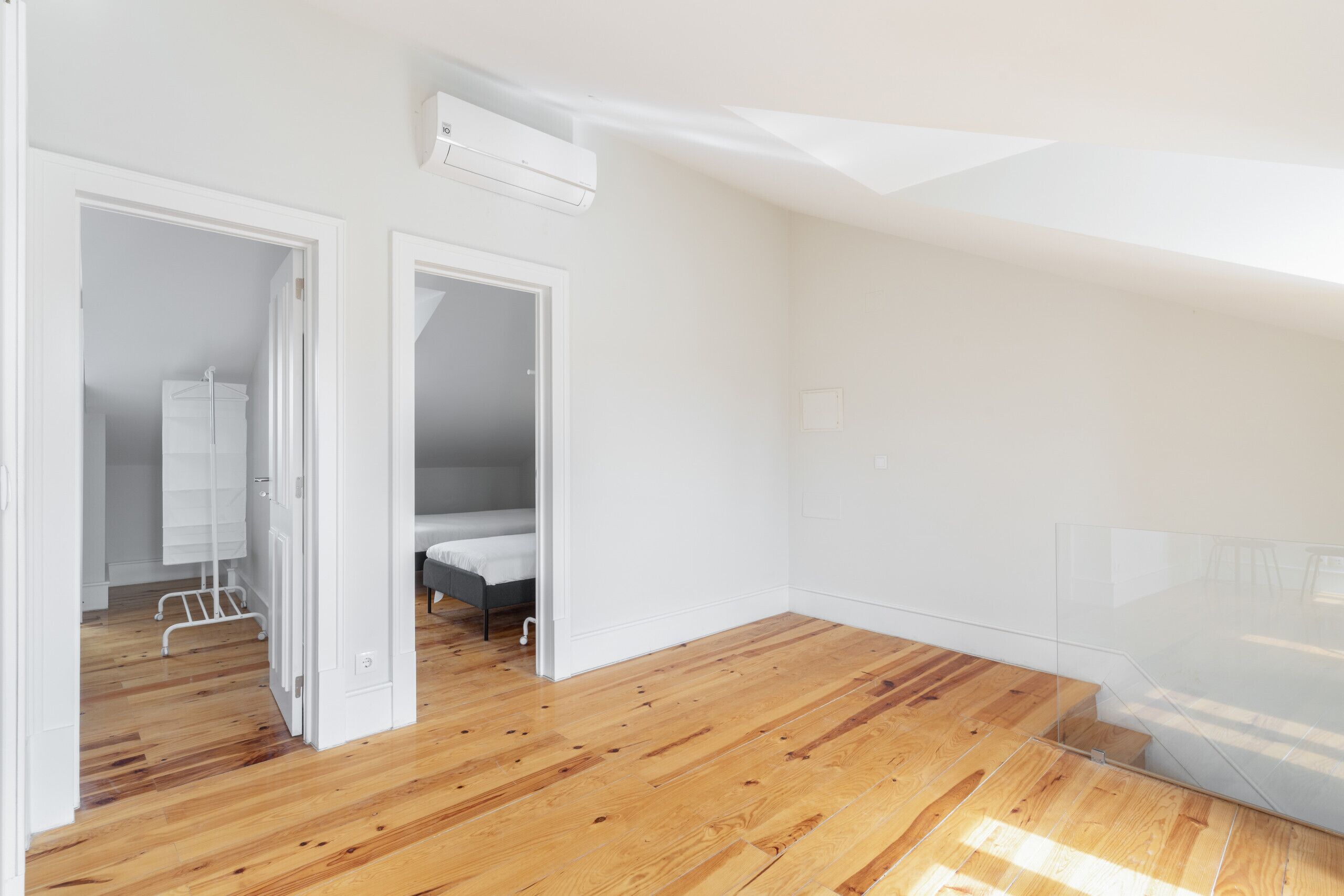 A room with wooden flooring, white walls, a bed, and a white wardrobe.