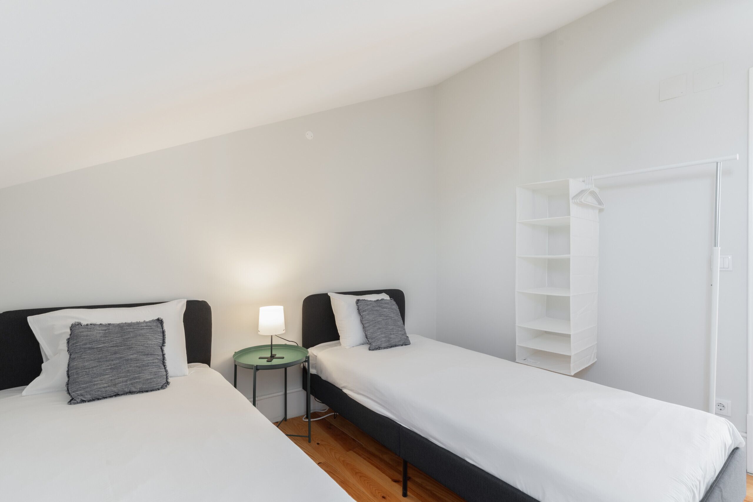 Un dormitorio con dos camas, una mesita de noche con lámpara y un armario blanco.