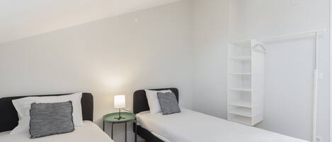 Un dormitorio con dos camas, una mesita de noche con lámpara y un armario blanco.