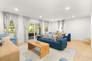 Ein modernes Wohnzimmer mit einem blauen Sofa, einem Holztisch und einem Essbereich im Hintergrund.