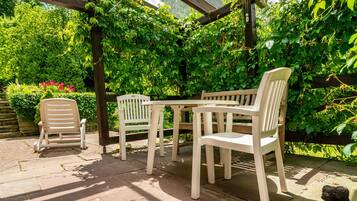Een overdekt terras met een tafel en stoelen, omgeven door weelderige begroeiing.