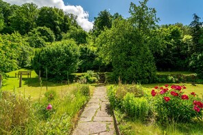 Ein gepflasterter Weg schlängelt sich durch einen üppigen Garten mit einer Bank und einem Tor.