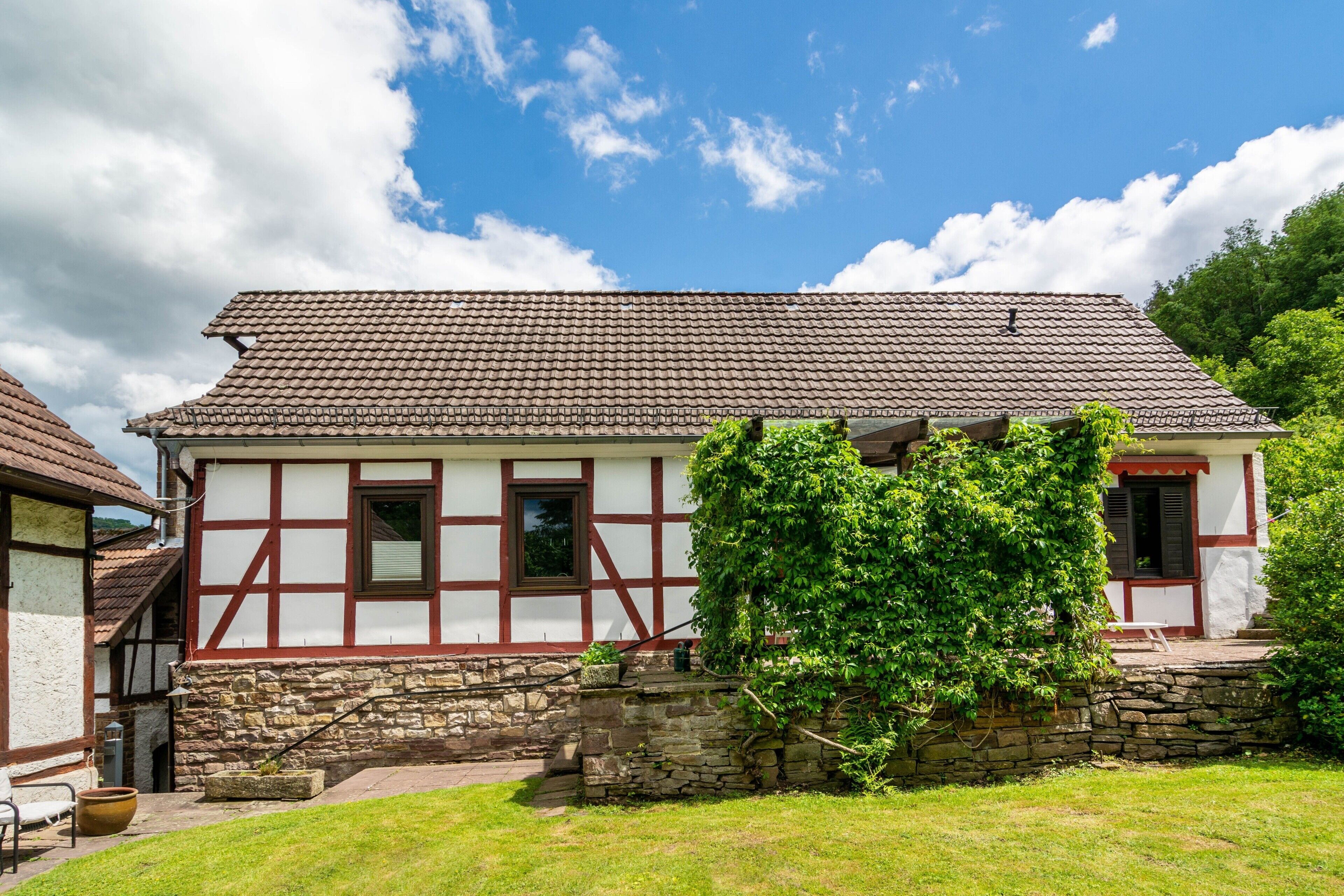 Ett traditionellt hus med korsvirkesfasad, ett fundament av sten, ett tak täckt med tegelpannor och en liten trädgård.