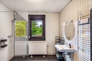 A modern bathroom with a glass shower enclosure, a white sink with a mirror, and a view of greenery outside. - Holiday Home 'Am Ritzberg' with Private Terrace, Shared Garden and Sauna (Beverungen)