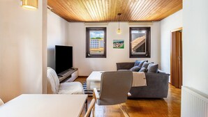 Una sala de estar moderna con techo de madera, un televisor de pantalla plana, un sofá gris, un escritorio blanco y una silla.