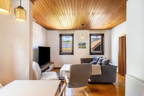 A modern living room with a wooden ceiling, a flat-screen TV, a gray sofa, a white desk, and a chair. - Holiday Home 'Am Ritzberg' with Private Terrace, Shared Garden and Sauna (Beverungen)