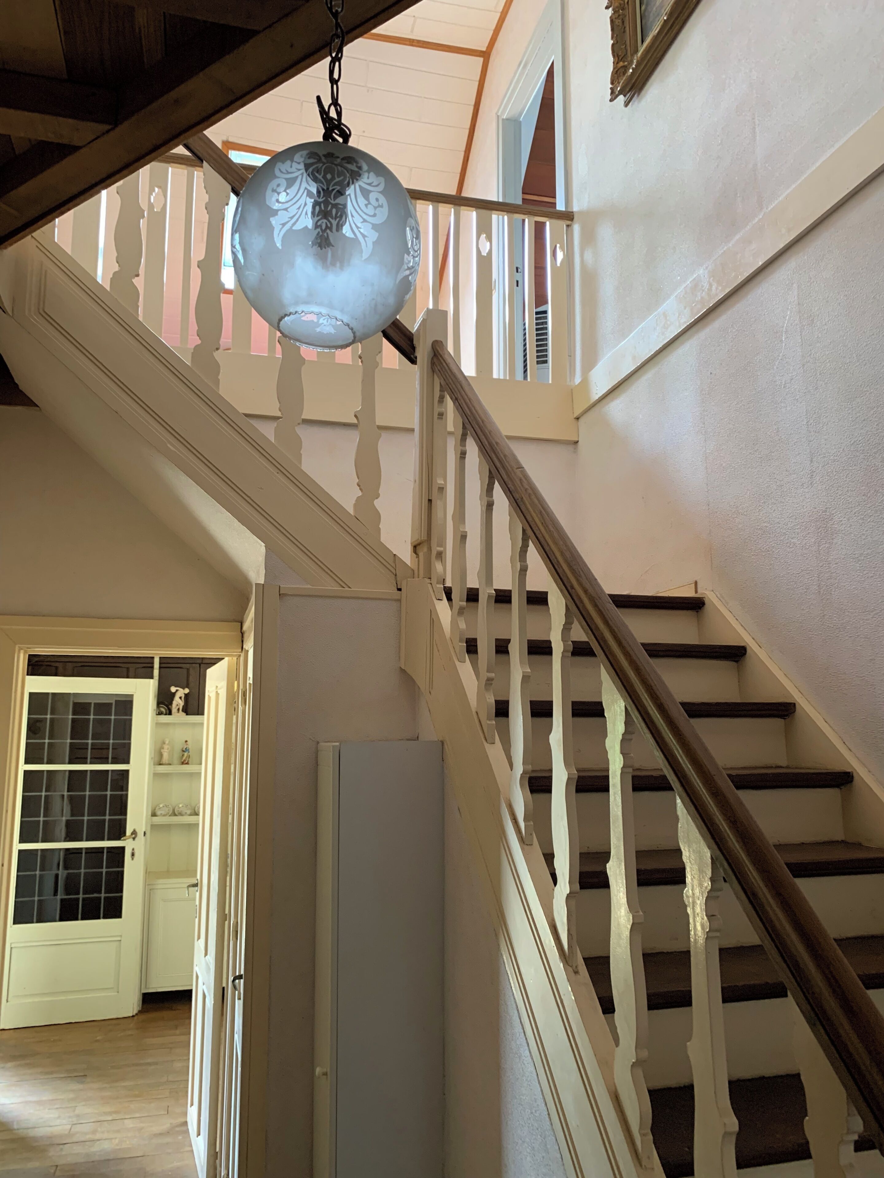 Uma escadaria com corrimão de madeira, uma porta branca com painéis de vidro e um lustre.
