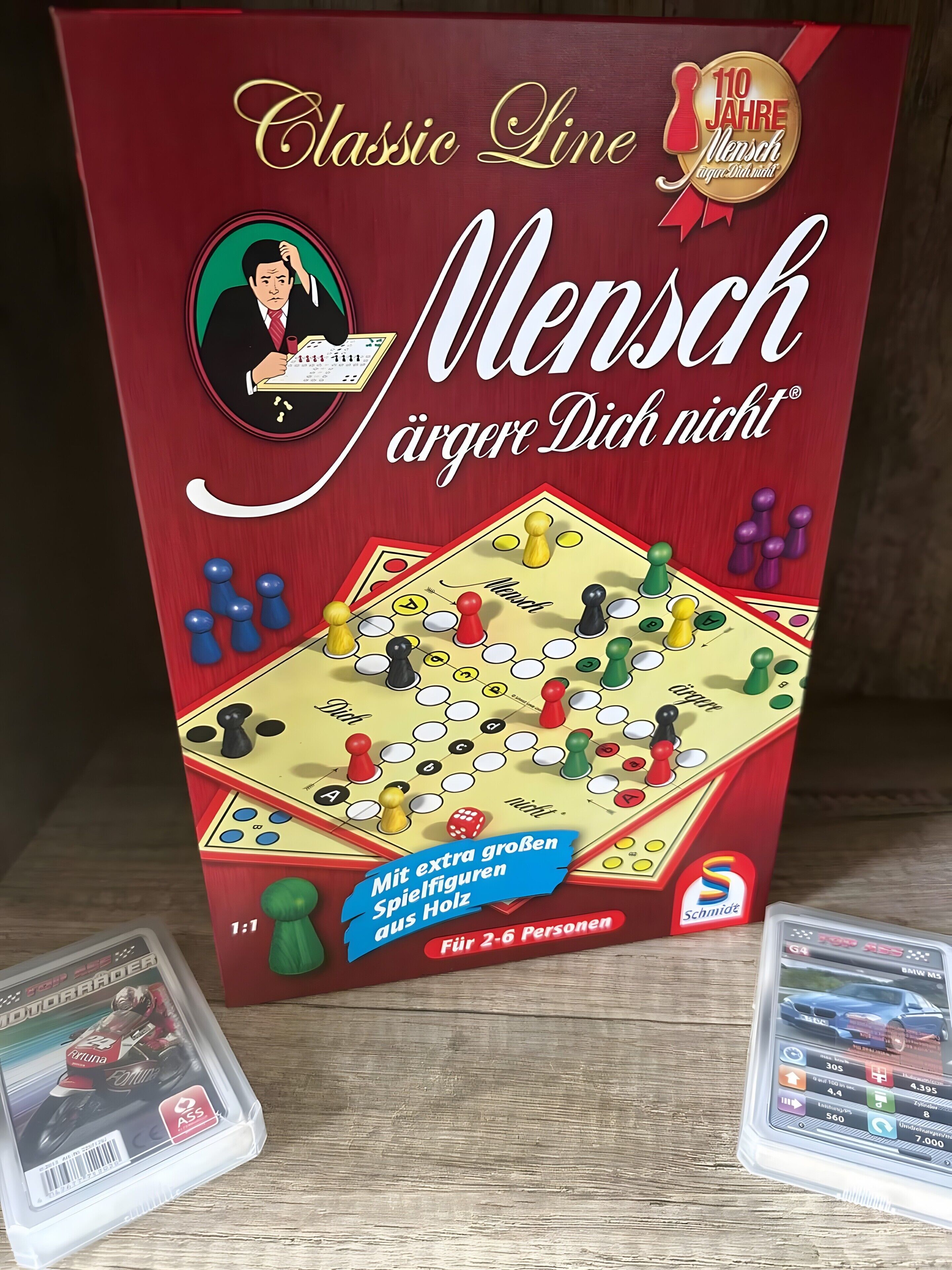 Un juego de mesa titulado 'Classic Line Mensch Jäger Dich nicht' con un emblema conmemorativo del 110 aniversario, diseñado para 2 a 6 jugadores, e incluye piezas de madera extra grandes.