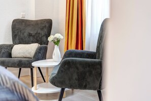 Ein modernes Zimmer mit zwei grau gepolsterten Sesseln, einem kleinen weißen Tisch und einer Vase mit weißen Blumen.