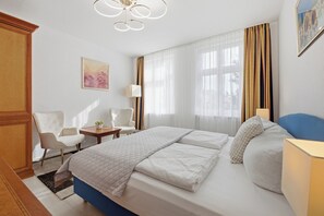 Ein Hotelzimmer mit einem Bett, zwei Stühlen, einem Schreibtisch, einer Lampe und einem Bild an der Wand.