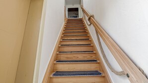 Een houten trap met een leuning, die leidt naar een kamer met een wit plafond en een zichtbare deur.