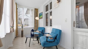 Een kamer met twee blauwe fauteuils, een kleine ronde tafel, een vaas met bloemen en een schilderij aan de muur.