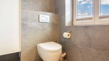 Un baño moderno con inodoro, un bidé adosado a la pared y ventana con vista al cielo.