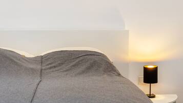 A bed with grey bedding, a white wall, and a nightstand with a black lamp.