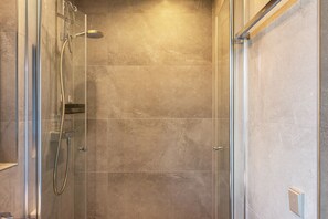 Eine begehbare Dusche mit Glaswänden, einer Handbrause und einem an der Wand befestigten Wasserhahn.