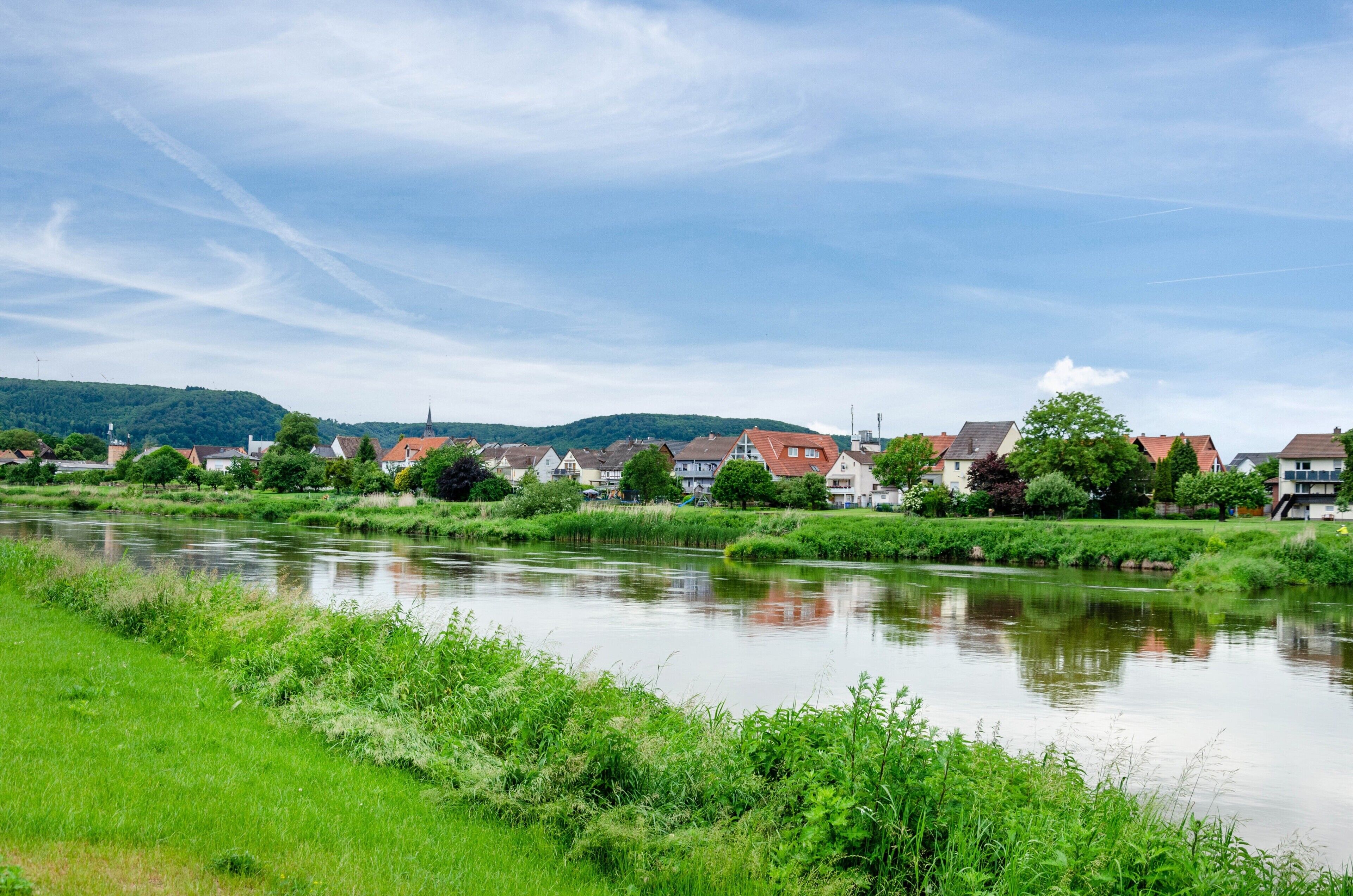 Ein Fluss mit Häusern am gegenüberliegenden Ufer, ein klarer Himmel und Grün entlang des Flussufers.