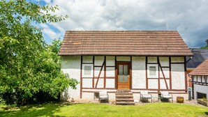 A traditional half-timbered house with a tiled roof, a wooden door, and a small porch with outdoor seating. - Holiday Home "Am Ritzberg 2" with Shared Garden and Wi-Fi (Beverungen)