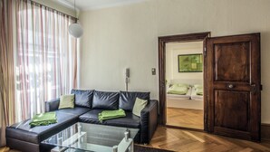 Ein modernes Wohnzimmer mit einem Glastisch, einem dunkelbraunen Ledersofa, Holzboden und einer Tür zu einem anderen Raum.