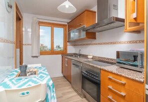A compact kitchen with a stove, oven, microwave, and a window with curtains. - Apartment Son Baulo Poma (Can Picafort)