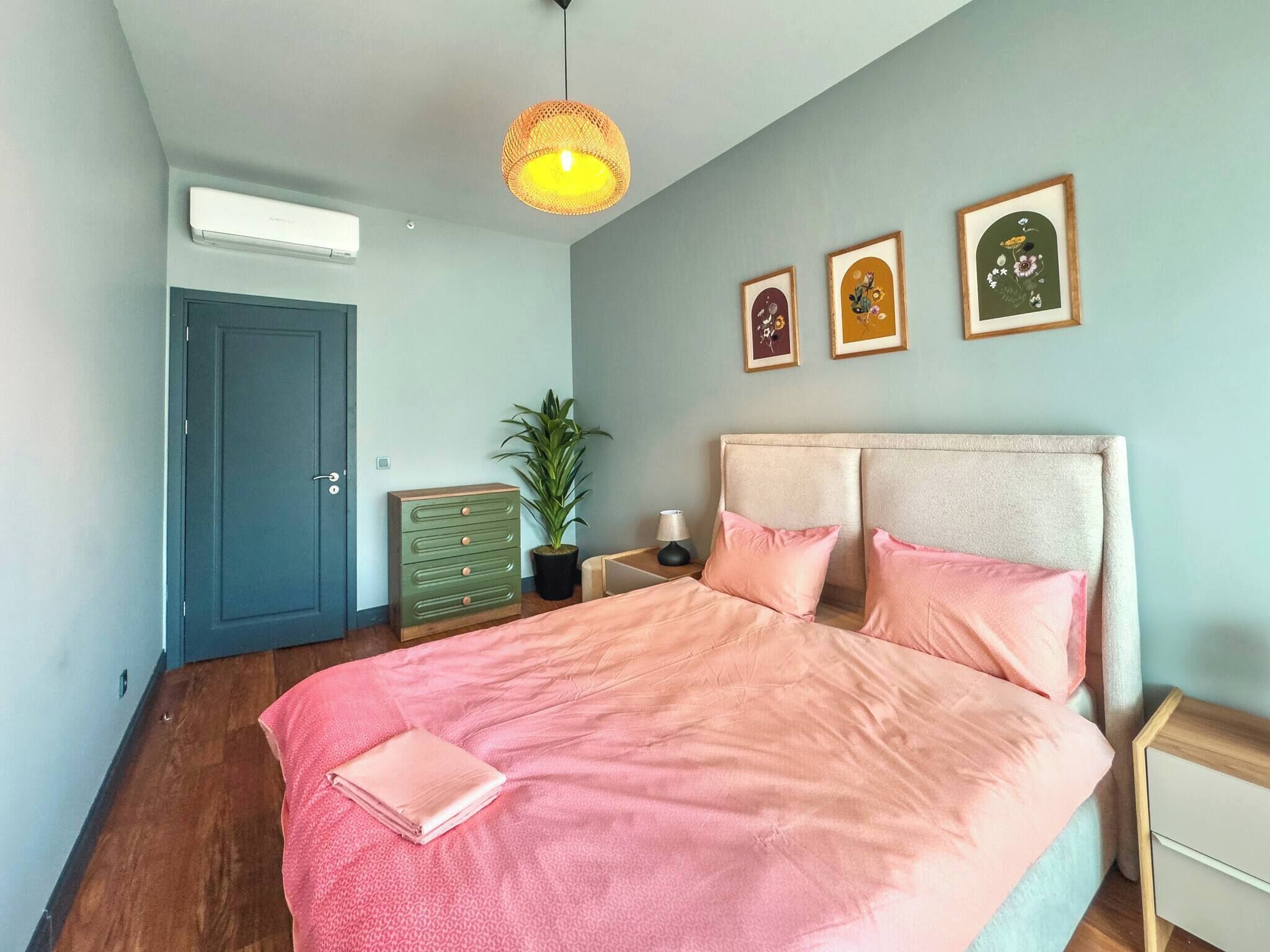 Quarto com cama, cômoda, planta, porta e arte nas paredes.