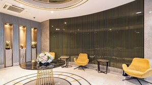 Eine moderne Lobby mit Marmorboden, einem runden Tisch in der Mitte und einer Blumenkomposition sowie zwei gelben Sessel.