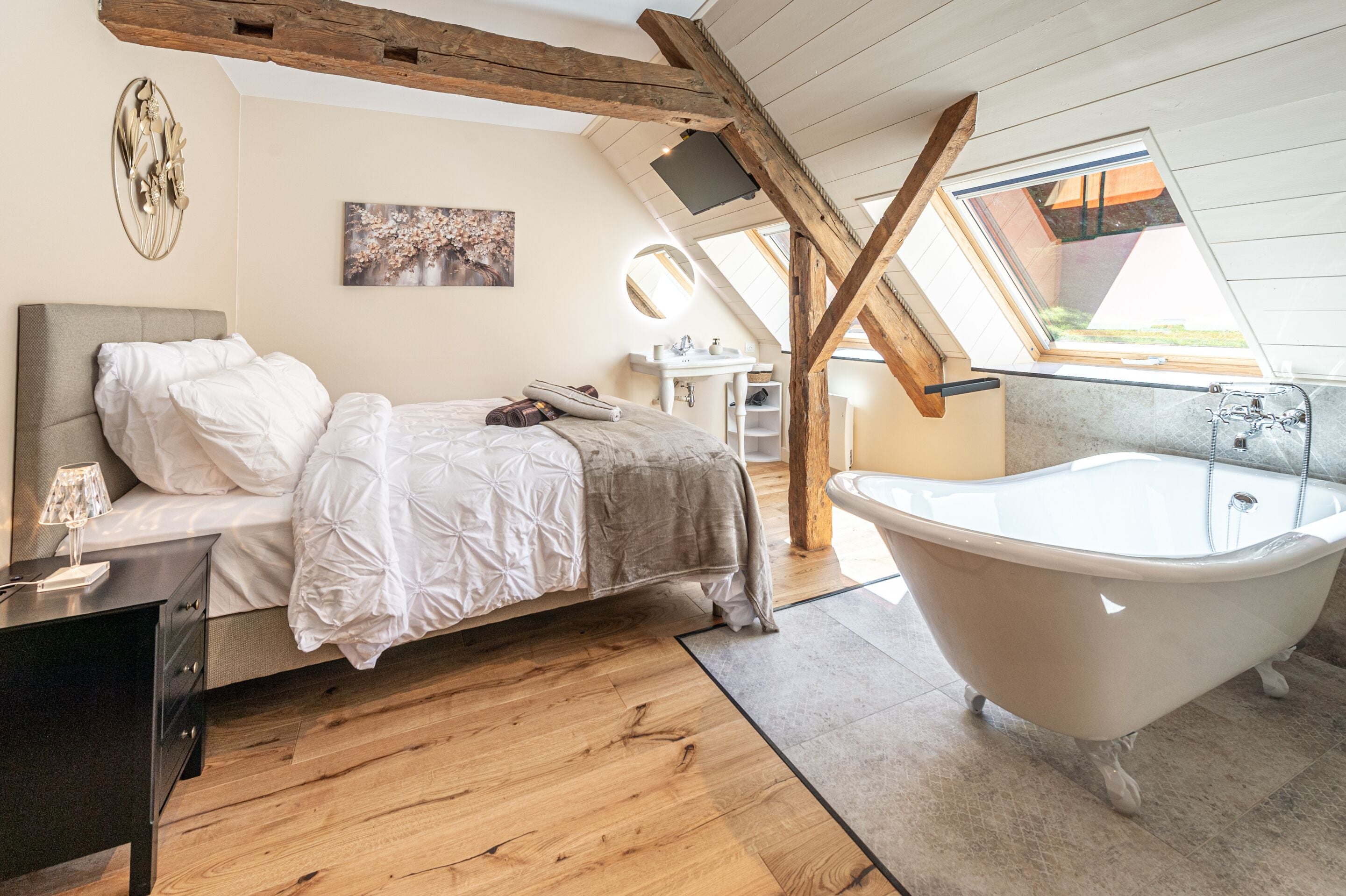 Ein Schlafzimmer mit Bett, Schminktisch, Badewanne, Holzbalken und einem Oberlicht.