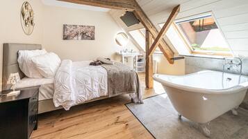 Ein Schlafzimmer mit Bett, Schminktisch, Badewanne, Holzbalken und einem Oberlicht.