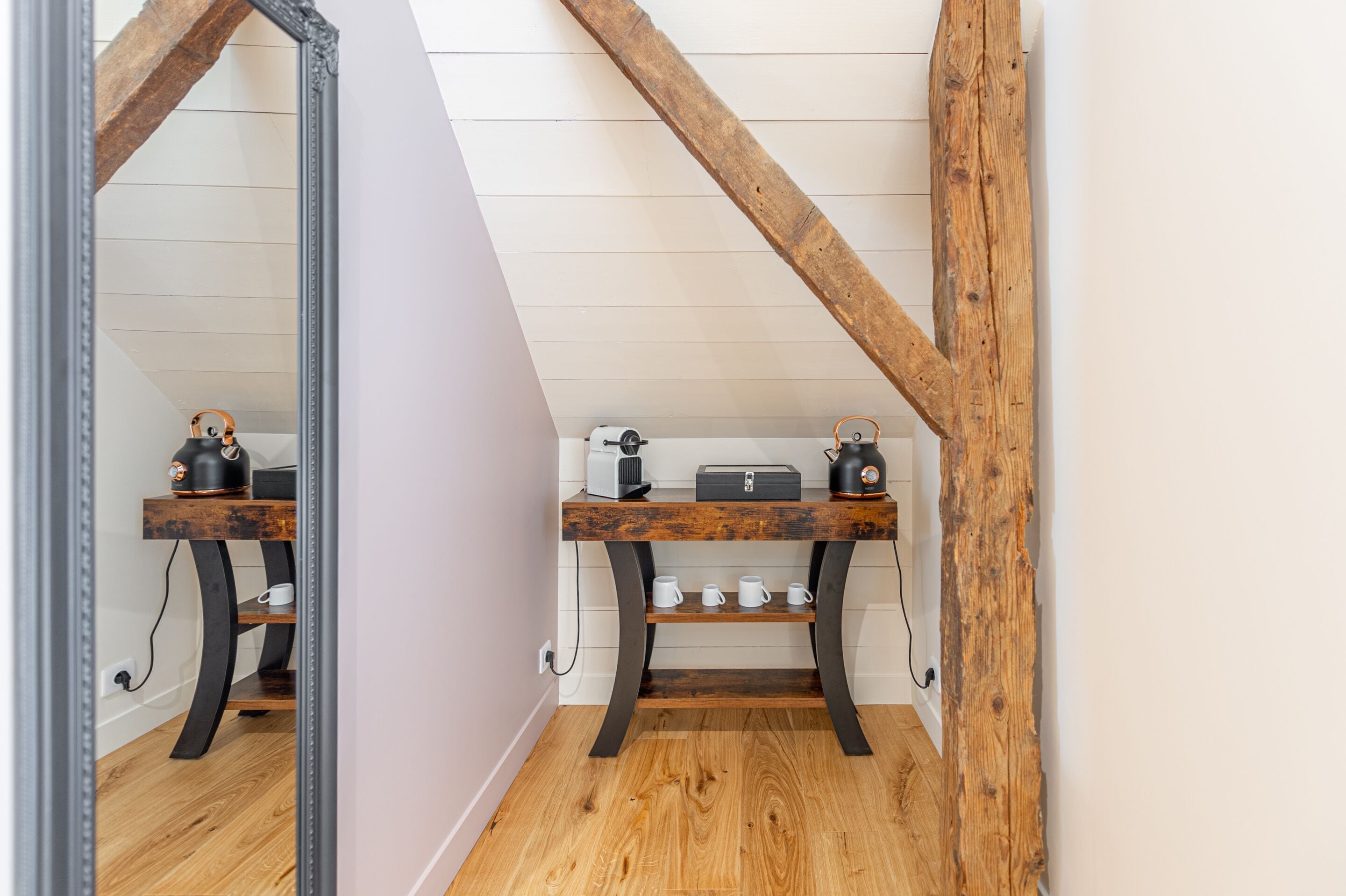 A room with a wooden floor, a mirror, a wooden bench, and a small table with a kettle and cups.