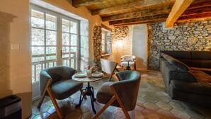 A rustic interior with stone walls, wooden beams, a stone fireplace, and a seating area with chairs and a sofa. - Le Moulin de mes garçons (Alby-sur-Chéran)