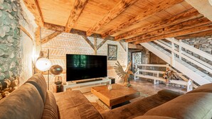 A cozy living room with a large flat-screen TV, comfortable sofas, a wooden coffee table, and a stone wall. - Le Moulin de mes garçons (Alby-sur-Chéran)