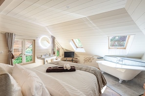 A bedroom with a large bed, a bathtub, a TV, and a window.
