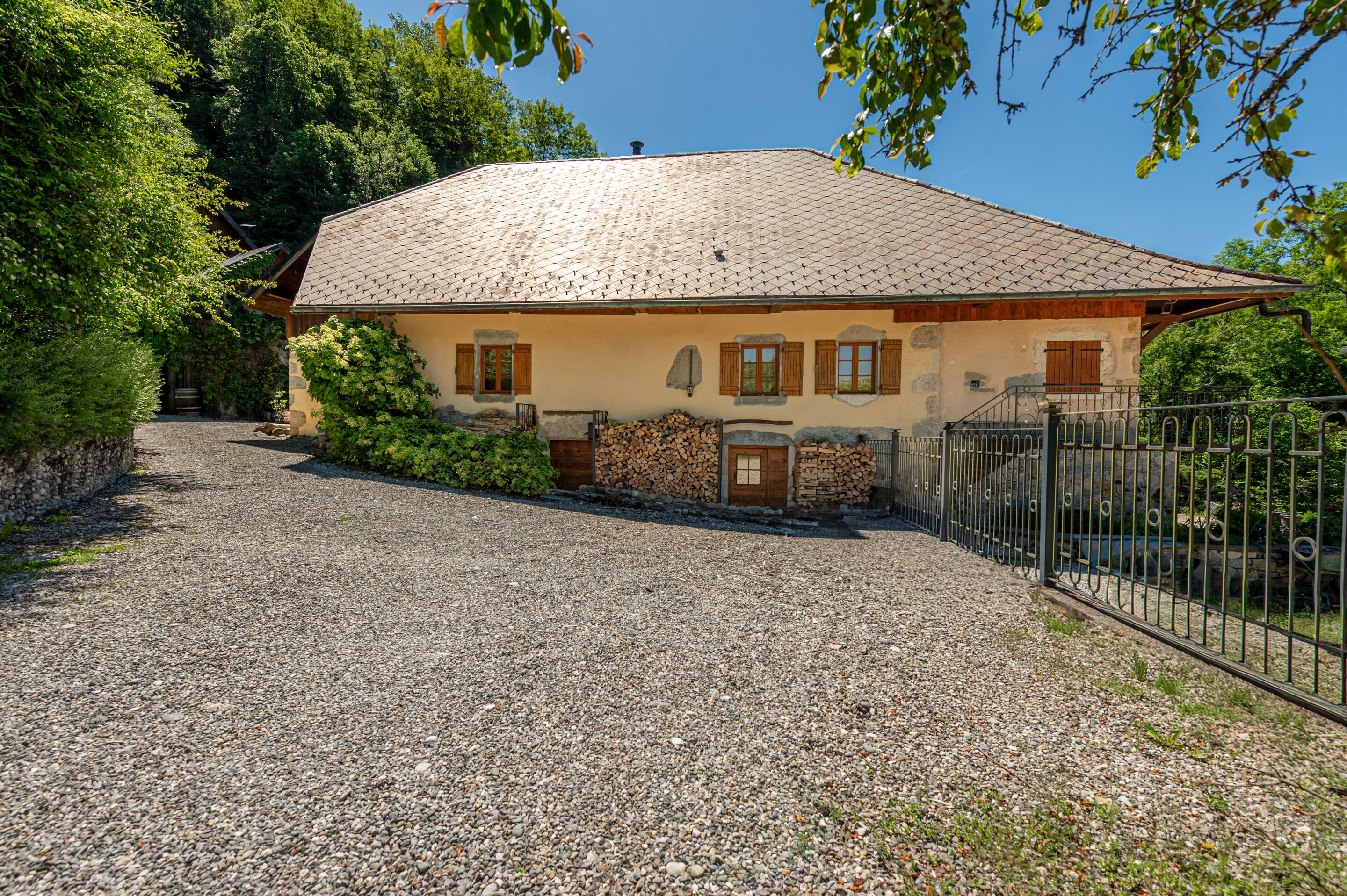 A house with a gravel driveway, wooden shutters, and a metal fence.