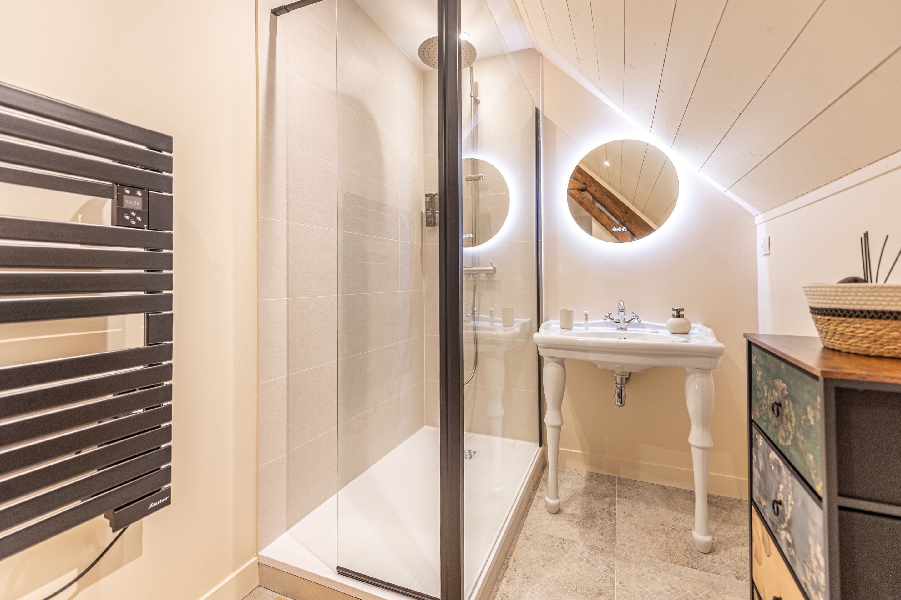 A modern bathroom with a glass shower enclosure, a white pedestal sink, and a wooden ceiling.