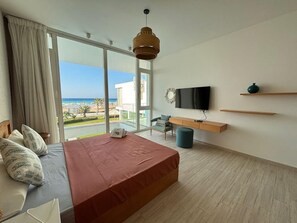 Quarto com cama, escrivaninha, cadeira, televisão e vista para o mar.