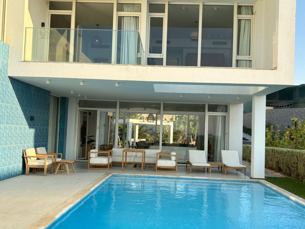 A modern two-story building with a swimming pool, outdoor seating, and large windows.