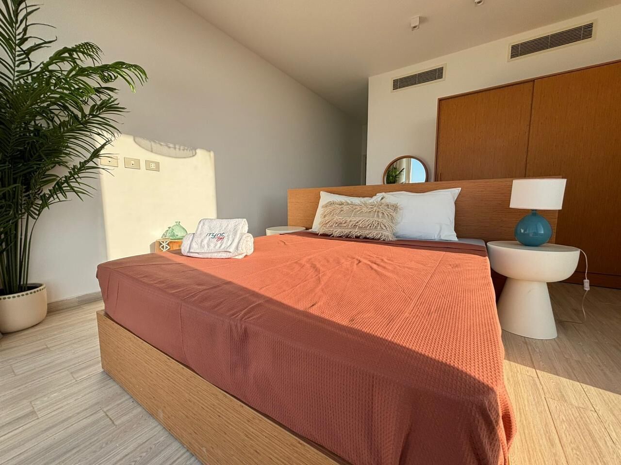 Une chambre à coucher avec un grand lit, une table de chevet, une commode, une plante en pot et une armoire.