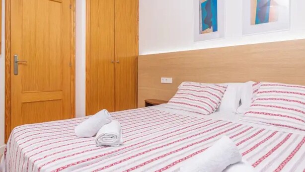 A hotel room with a bed, two wooden doors, and two framed artworks on the wall. - Apartment Son Baulo Poma (Santa Margalida)