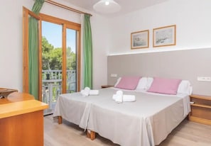 Habitación de hotel con cama, escritorio, balcón con cortinas y dos cuadros en la pared.