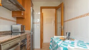 A compact kitchen with a microwave, refrigerator, oven, and a dining area with a table set for two. - Apartment Son Baulo Poma (Santa Margalida)