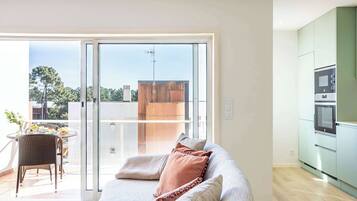Ein modernes Wohnzimmer mit einer Couch, einer Schiebetür zum Balkon und einer Küchenzeile.