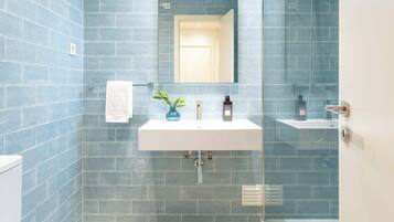 Ein Badezimmer mit weißem Waschbecken, Spiegel und Toilette, mit blauen Fliesen und einer Duschkabine aus Glas.