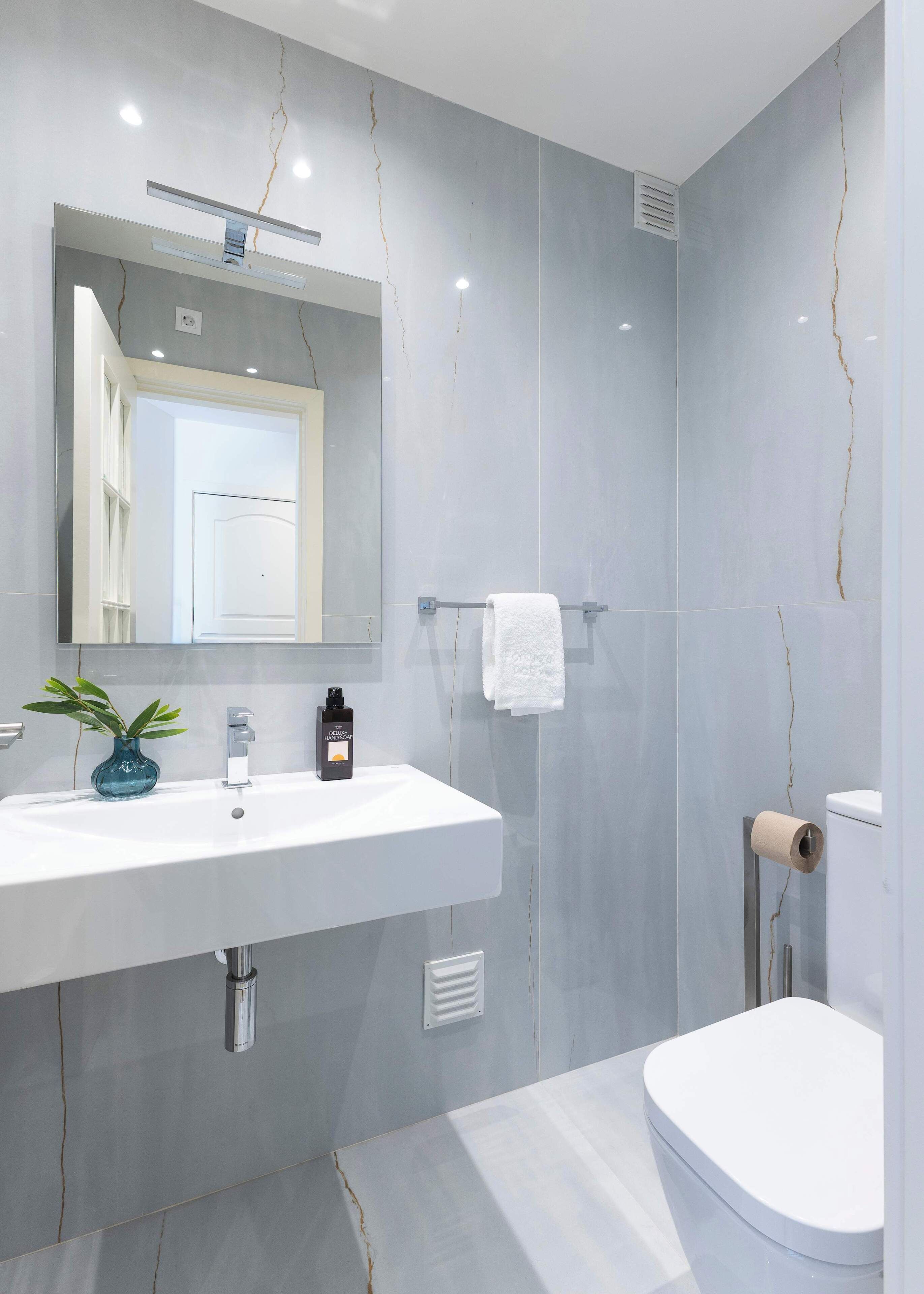 Een moderne badkamer met een witte wastafel, spiegel en toilet.