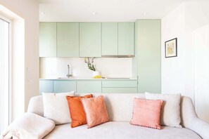 Ein modernes Wohnzimmer mit einer Couch, einer Küchenzeile mit grünen Schränken und einem gerahmten Bild an der Wand.